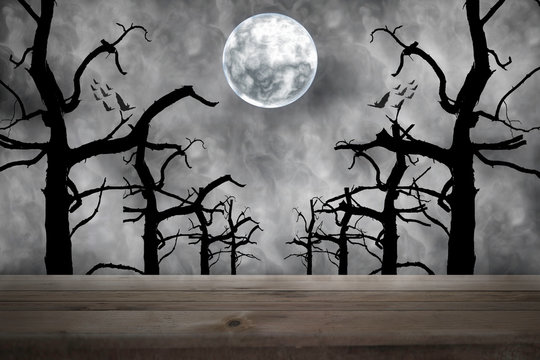 Halloween background. Spooky forest with dead trees and wooden table. Full moon night.
