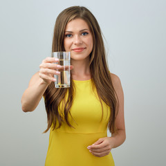 woman in casual yellow dress holding water glass in front of her.