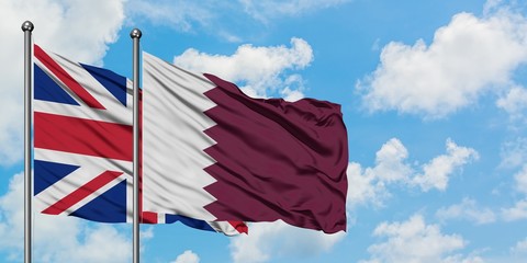 United Kingdom and Qatar flag waving in the wind against white cloudy blue sky together. Diplomacy...