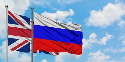 United Kingdom and Russia flag waving in the wind against white cloudy blue sky together. Diplomacy concept, international relations.
