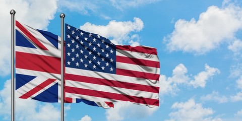 United Kingdom and United States flag waving in the wind against white cloudy blue sky together. Diplomacy concept, international relations.