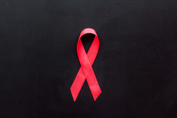 Pink ribbon as symbol of breast cancer awareness on black background top view copy space