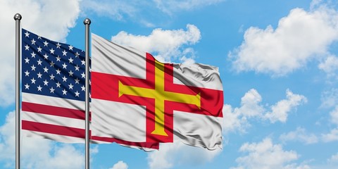 United States and Guernsey flag waving in the wind against white cloudy blue sky together. Diplomacy concept, international relations.