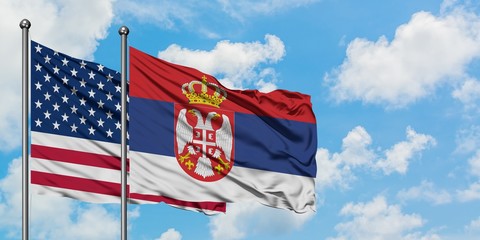 United States and Serbia flag waving in the wind against white cloudy blue sky together. Diplomacy concept, international relations.