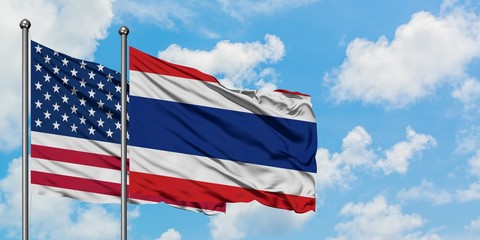 United States and Thailand flag waving in the wind against white cloudy blue sky together. Diplomacy concept, international relations.