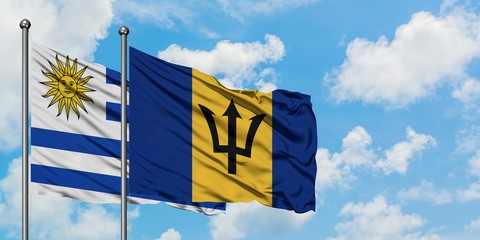 Uruguay and Barbados flag waving in the wind against white cloudy blue sky together. Diplomacy concept, international relations.