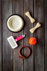 Set of treats and toys for pets with bones, collar and bowl on dark wooden background top view