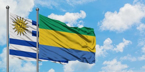 Uruguay and Gabon flag waving in the wind against white cloudy blue sky together. Diplomacy...
