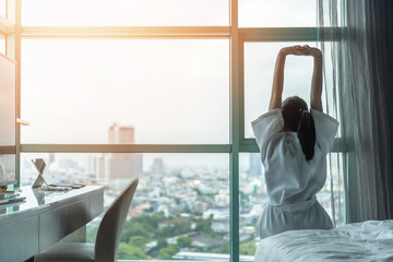 Work-life quality balance concept with happy city lifestyle Asian girl having a good day waking up from sleep in morning taking some rest, lazily relaxing in comfort in condominium or hotel bed room