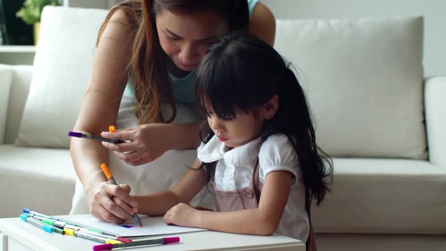 Young mother teaching her daughter painting colour pencil on paper