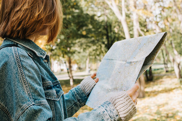 Lifestyle portrait of young adult female in a forest or park holding map in her hands, selective focus