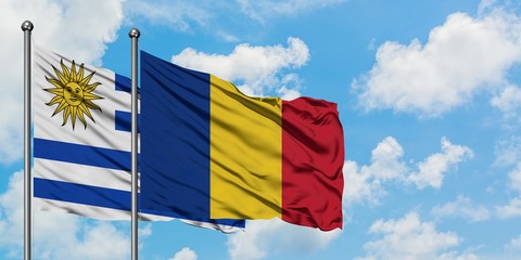 Uruguay and Romania flag waving in the wind against white cloudy blue sky together. Diplomacy concept, international relations.