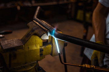Worker welding and heating a metal bar motorcycle part using a machine. close-up.