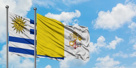 Uruguay and Vatican City flag waving in the wind against white cloudy blue sky together. Diplomacy...