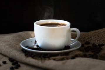 A steaming cup of coffee with coffee beans on vintage wooden table.