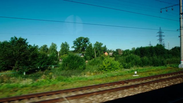 High-speed Train moves past a village and a station in the summer