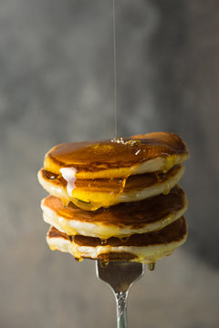 Tasty breakfast. Homemade stack pancakes on fork with  honey or maple syrup on  grey  background.