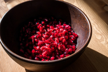 Pomegranate Seeds in Wooden Bowl with  Natural Sunlight and Pastel Yellow Tablecloth. Natural Sunlight.