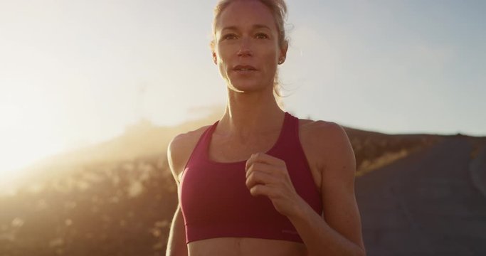 Strong attractive woman running at sunset with golden cloud haze atmosphere, amazing sunset workout in the mountains, determined runner training at sunset