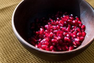 Pomegranate Seeds in Wooden Bowl with  Natural Sunlight and Pastel Yellow Tablecloth. Natural Sunlight.