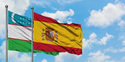 Uzbekistan and Spain flag waving in the wind against white cloudy blue sky together. Diplomacy concept, international relations.