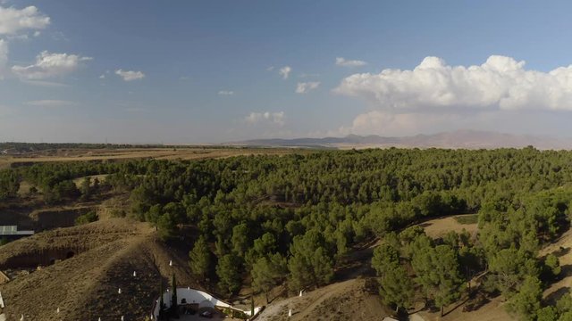 Green dense forest in Aerial drone shot in countryside in dry desert with green vegetation and mountains in Andalusia. Cloudy Blue sky, Almeria, Spain. During the day. Trees 4K UHD.