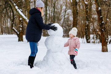 mom and daughter make a snowman out of snow