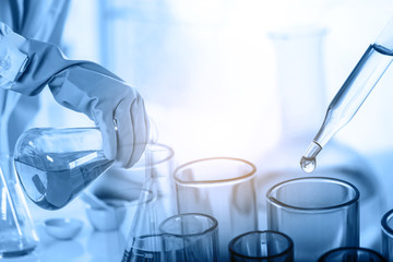 hand of scientist holding flask with lab glassware and test tubes in chemical laboratory background, science laboratory research and development concept