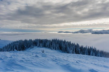 Beautiful scenery with winter snow-capped mountains, with fogs and contrasting snow structure and red tourist tent in the foreground, in locations in the Ukrainian Carpathians.