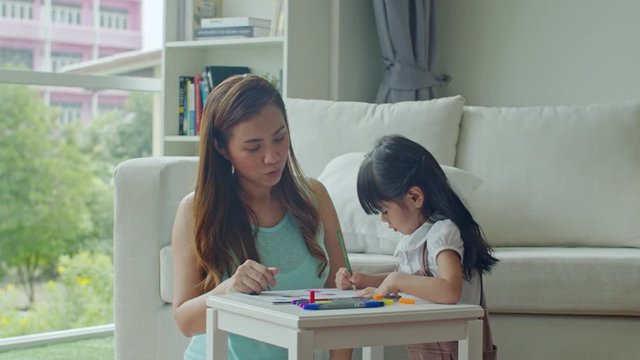 Cheerful young mother looking daughter drawing on paper
