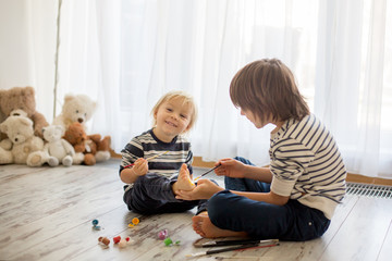 Naklejka premium Brothers, playing at home, painting on their feet, tickling, laughing, smiling