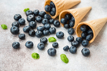 Blueberries lie in a waffle cone and scattered on a concrete table. Summer seasonal product. Healthy vegetarian dessert.