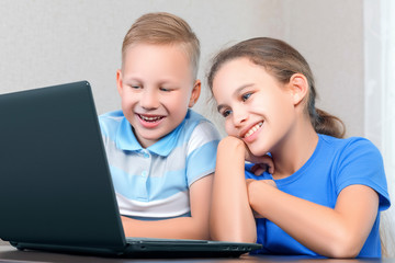 Children at the computer. Little cute boy and little beautiful girl look at the laptop screen and smile cute. Distance learning, fun leisure concept. Happy children use a laptop.