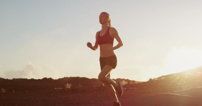 Fit attractive woman running at sunset with golden cloud haze atmosphere, amazing sunset workout in the mountains, determined runner training at sunset achieving her fitness goals
