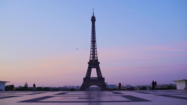 Eiffel tower at sunset orange blue sky in Paris during the summer. Haussmanian buildings, trees, 16th, symbol, trocadero, architecture, landmark, historic. Static Wide shot 4K UHD.