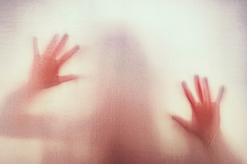 Shadow of scary paranormal ghost horror woman behind the matte red glass in soft focus. Blurry hand...