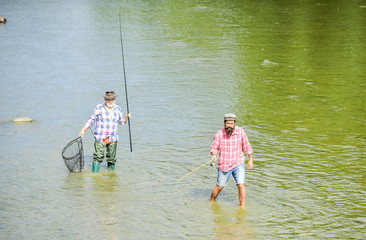 Teach man to fish and you feed him for lifetime. Male friendship. Father and son fishing. Summer weekend. Happy fisherman with fishing rod and net. Hobby and sport activity. Fishing together