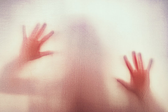 Shadow of scary paranormal ghost horror woman behind the matte red glass in soft focus. Blurry hand and body figure abstraction.