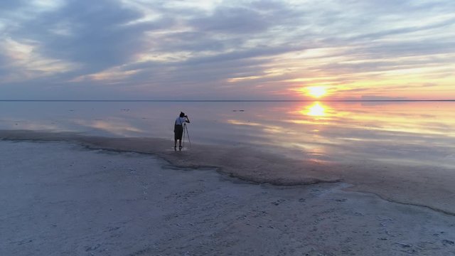 Flight around photographer with tripod. Beautiful wooman girn noface. Sunset salt mineral lake Elton Russia. Clouds sun reflection in water landscape horizon.  Tourism travel Europe best landmark. 