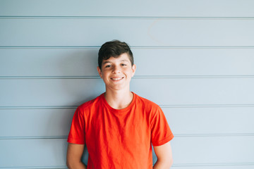 Portrait of a cheerful male teen leaning on wood wall while looking camera