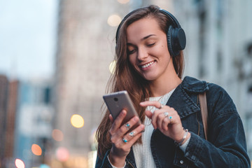 Young happy stylish trendy casual hipster woman changes songs and tracks on smartphone during...