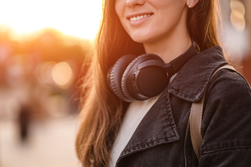 Stylish casual fashionable hipster student woman teenager with black wireless headphones while walking around the city. Lover music enjoys listening music