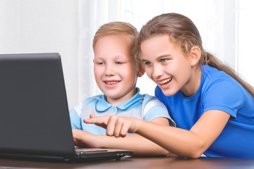 Two beautiful cute happy smiling children, a boy and a girl, use laptop for distance learning or entertainment. Children look at the screen with interest and the girl points with the finger to display