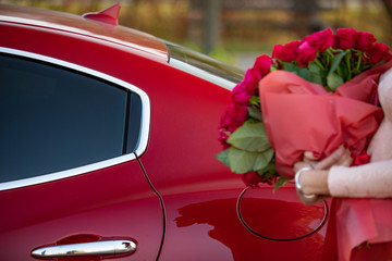 Woman near the car with beautiful bouquet of roses in hands. Holidays and celebration concept.
