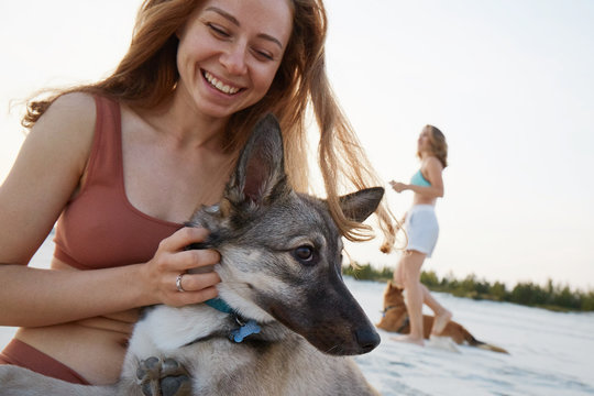 A girl hugging her dog on the beach in sunset laughing
