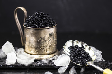 black caviar in  mug  with black caviar spoon on dark moss background. .Free space for text. Black caviar. Luxurious culinary delicacy. Metal mug  and black caviar, closeup . © Maria