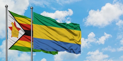 Zimbabwe and Gabon flag waving in the wind against white cloudy blue sky together. Diplomacy concept, international relations.