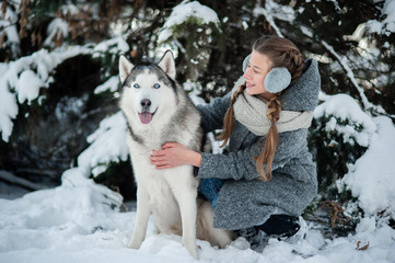 beautiful young girl in a gray coat in winter forest with Siberian Husky. Symbol of new year 2018