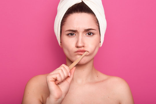 Close up portrait of attractive caucasian woman with dark hair posing isolated over pink background, femaklw with bare shouldersand white towel on head, lady looking at camera, brushing teeth.