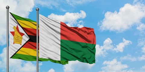 Zimbabwe and Madagascar flag waving in the wind against white cloudy blue sky together. Diplomacy concept, international relations.
